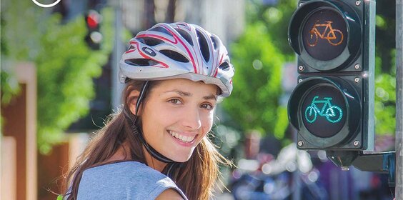 Junge Frau mit Fahrradhelm vor einer Ampel