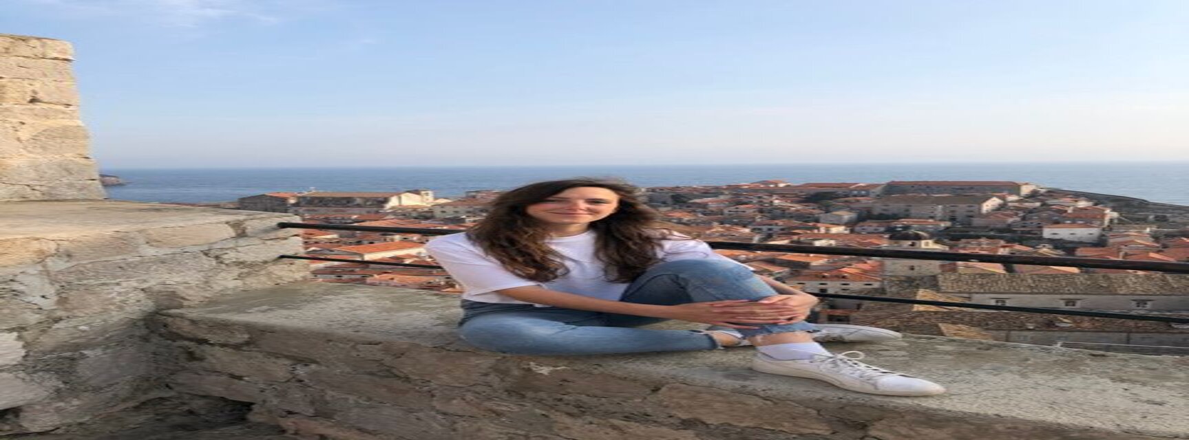 Girl sitting on a wall; Background city of Split