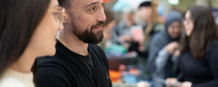 Eine Frau und ein Mann und Teilnehmende im Hintergrund.