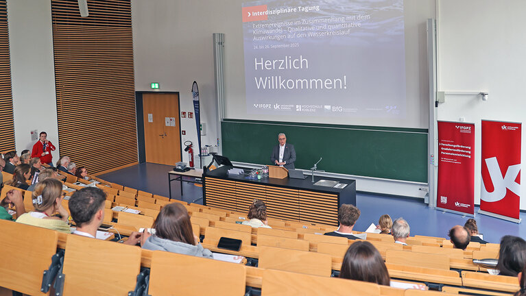 Mann begrüßt im Hörsaal Gäste zur Tagung
