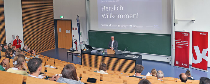 Mann begrüßt im Hörsaal Gäste zur Tagung