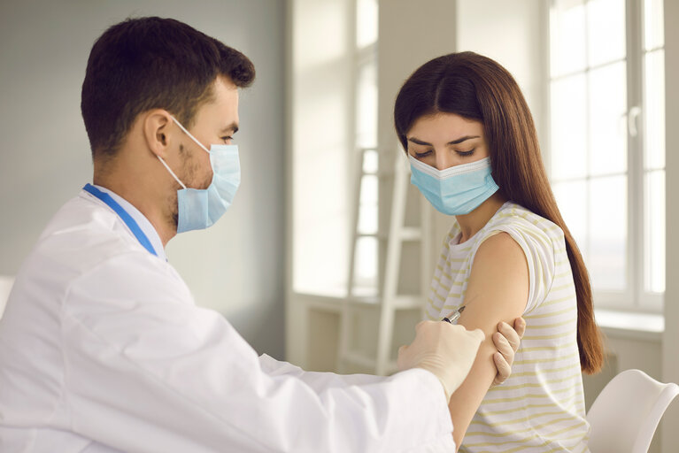 Male nurse giving vaccine to young woman during immunization campaign at health center