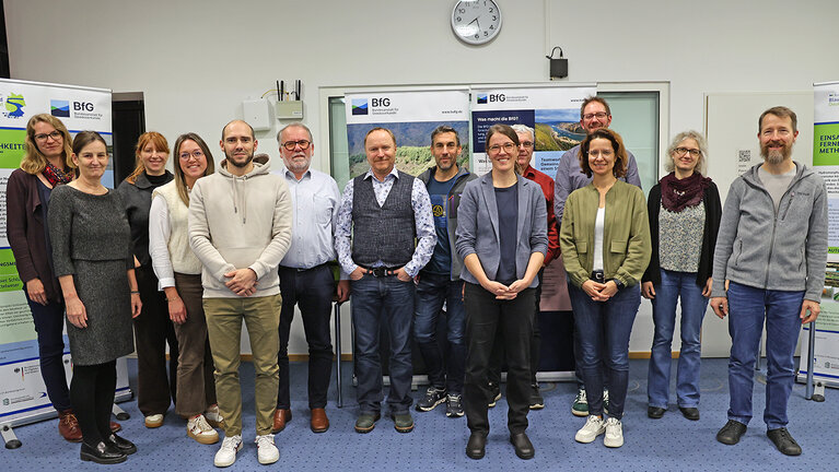 Eine Gruppe Menschen posiert für ein Gruppenbild. Im Hintergrund sind Rollups zu sehen.