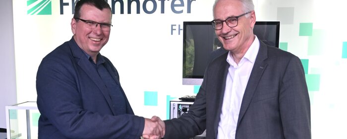 Zwei Herren schütteln sich die Hand vor einem Fraunhofer Plakat.