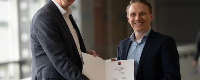 Zwei Männer stehen zusammen und halten eine Urkunde in ihrer Mitte.