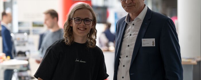 Ein Jugendlicher und ein Mann stehen zusammen und lächeln in die Kamera