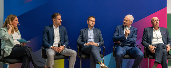 Eine Frau und vier Männer sitzen auf der Bühne im Rahmen einer Podiumsdiskussion.
