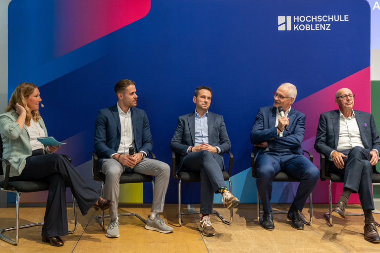 Eine Frau und vier Männer sitzen auf der Bühne im Rahmen einer Podiumsdiskussion.