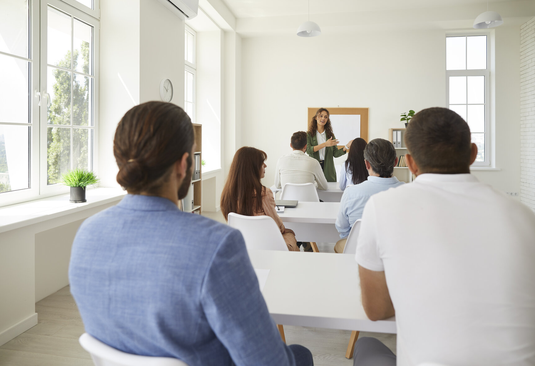 Group of adult students sitting at desks in classroom and listening to college teacher