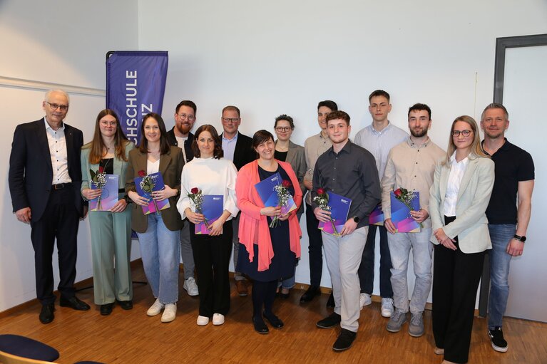 Bei einem Gruppenbild stehen Männer und Frauen zusammen vor einem Aufsteller der Hochschule Koblenz.