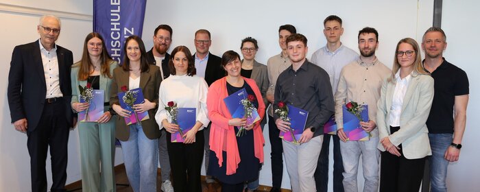 Bei einem Gruppenbild stehen Männer und Frauen zusammen vor einem Aufsteller der Hochschule Koblenz.