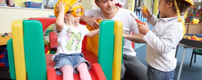 Ein Erzieher spielend mit zwei Kindern in der Kita.