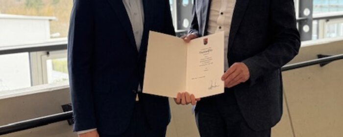 Zwei Männer stehen zusammen und halten eine Urkunde.