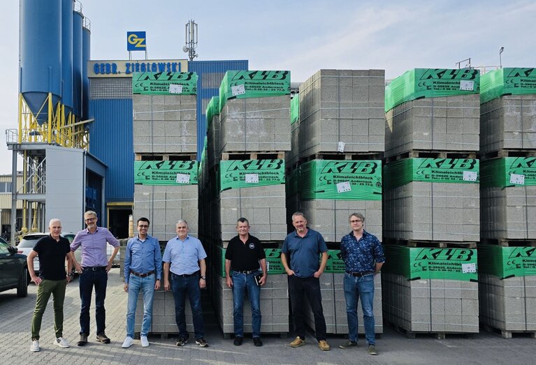 Sechs Männer stehen vor hohen Paletten mit Betonsteinen