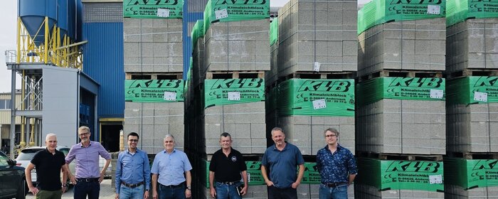 Sechs Männer stehen vor hohen Paletten mit Betonsteinen