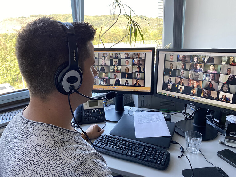 Mann mit Headset sitzt vor zwei Bildschirmen und nimmt an einer Online-Konferenz teil