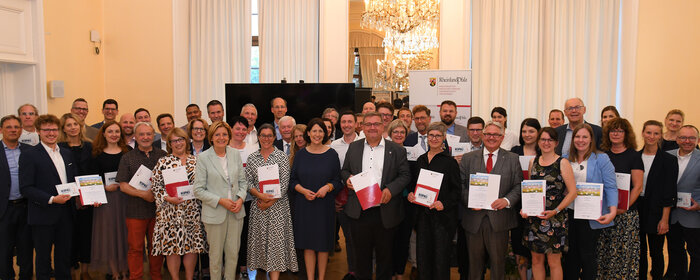 Eine Gruppe von Personen, die zum Teil Urkunden und Logoschilder in der Hand halten.