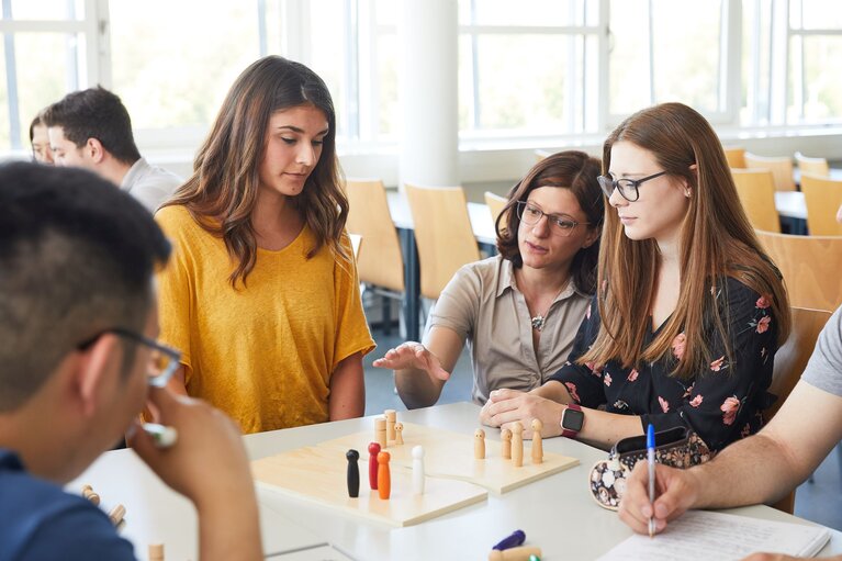 Studierende bei Gruppenarbeit mit Holzfiguren am Tisch.