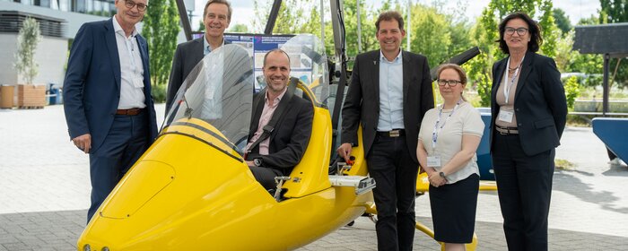 Eine Gruppe von Personen rund um den gelben Tragschrauber.