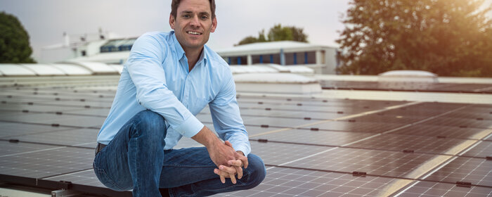 Ein Mann sitzt auf einem Dach mit Solarplatten.