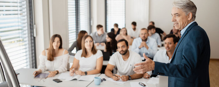 Studierende an Tischen im Vorlesungsraum und der Dozent Prof. Dr. Mühlencoert steht vorne und erklärt