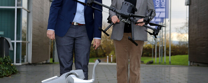 Ein Mann und eine Frau sowie ein vierbeiniger Roboterhund und eine Drohne.