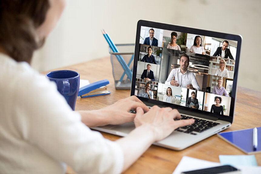 Frau vor Laptop. Auf dem Bildschirm sind mehrere Personen in einem Online Meeting zu sehen