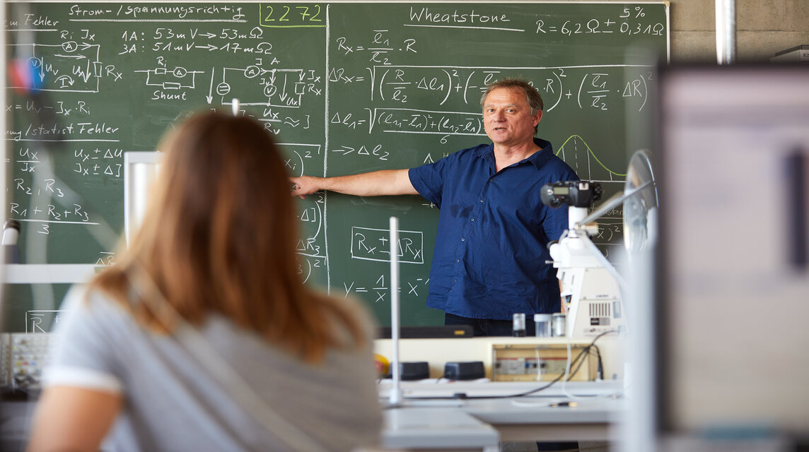 Professor vor Tafel mit mathematischen Formeln 