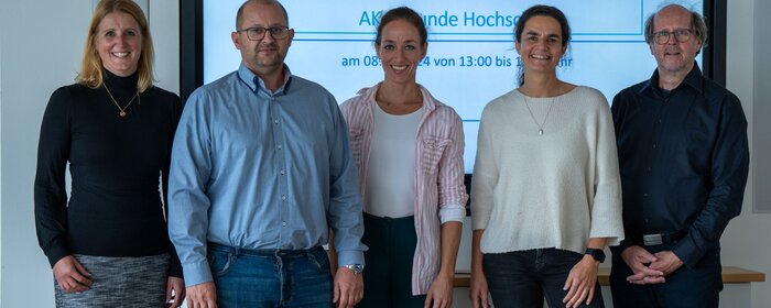 Eine Gruppe von 5 Personen steht vor einer Leinwand.