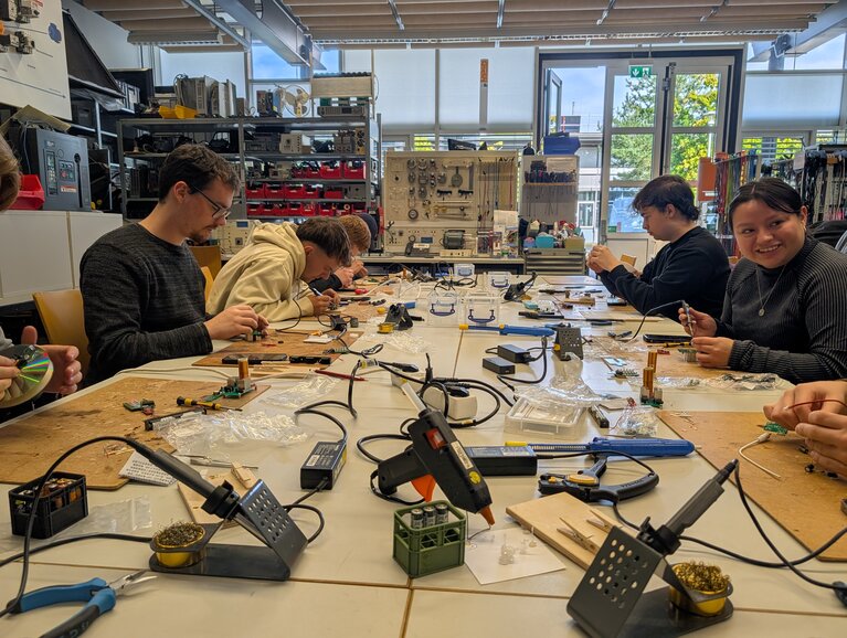 Anwendungsnahe elektronische Geräte selbst bauen Im einem Elektrolabor der Hochschule Koblenz sitzen sechs Studierende an einem Arbeitstisch. Sie arbeiten gemeinsam an elektronischen und elektrischen Versuchen. Im Workshop „DIY and Hands-on-Creators“ lernen sie durch praktisches Ausprobieren, wie die Technik hinter Alltagsgegenständen funktioniert.