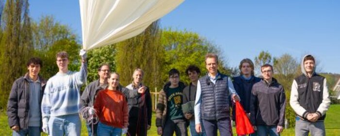 Die Teilnehmenden stehen auf einer Wiese und halten den Ballon, die Nutzlastsonde sowie den Fallschrim in der Hand.