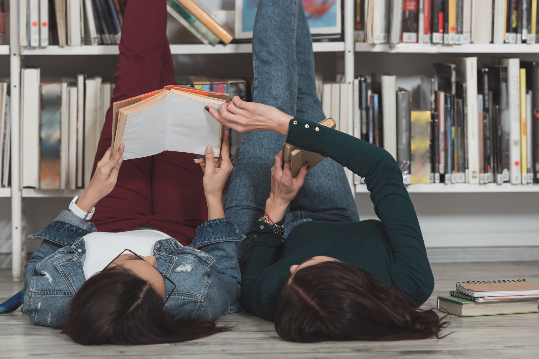 Imagebild: Zwei Personen liegen auf dem Boden, die Beine an ein Bücherregal gelehnt und lesen.