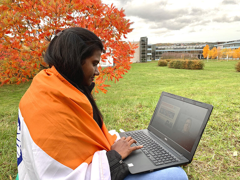 Austauschstudentin sitzt mit ihrem Laptop vor dem RheinAhrCampus auf der Wiese