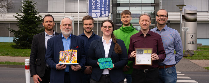 Eine Gruppe von sechs Männern und einer Frau steht zusammen. Drei von ihnen halten ein Modell in der Hand.