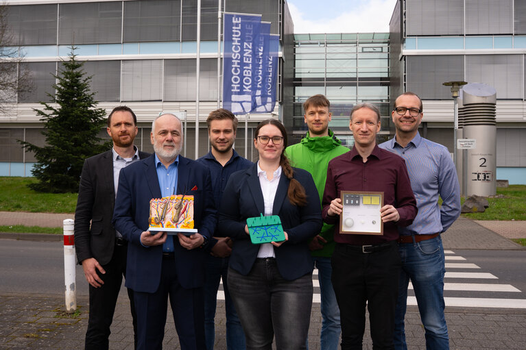 Eine Gruppe von sechs Männern und einer Frau steht zusammen. Drei von ihnen halten ein Modell in der Hand.