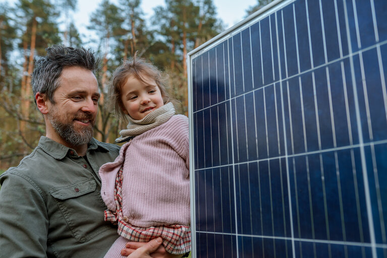 Portrait of father and daughter holding a solar panel in garden.