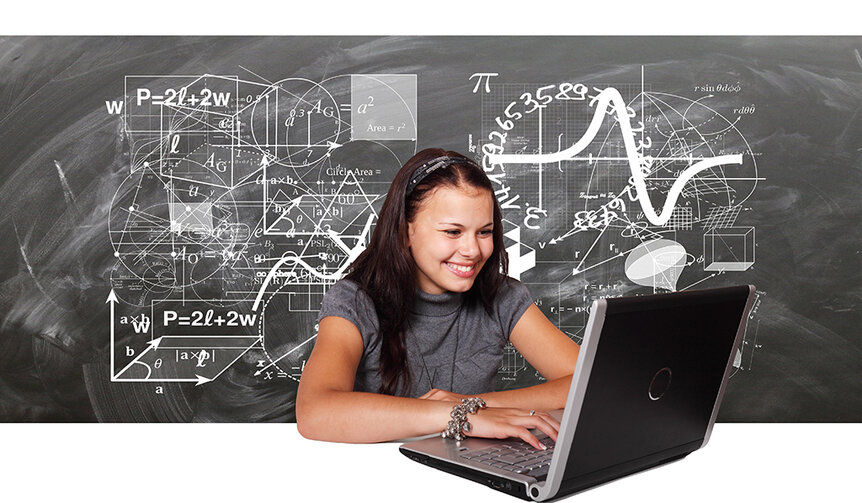 Studentin sitzt mit Laptop vor einer Tafel mit vielen mathematischen Formeln.