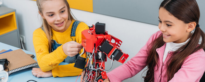 Zwei Mädchen experimentieren mit einem Roboter