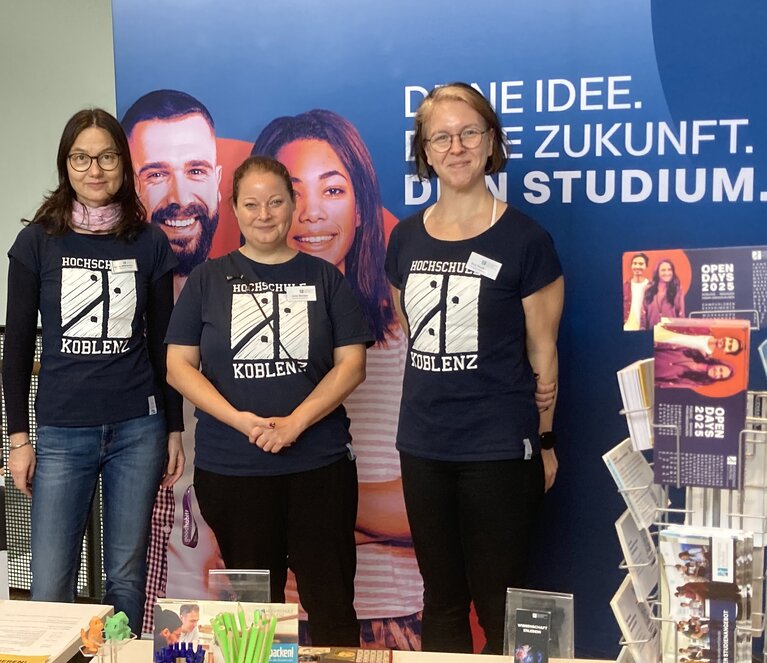Drei Frauen stehen an einem Projektstand.