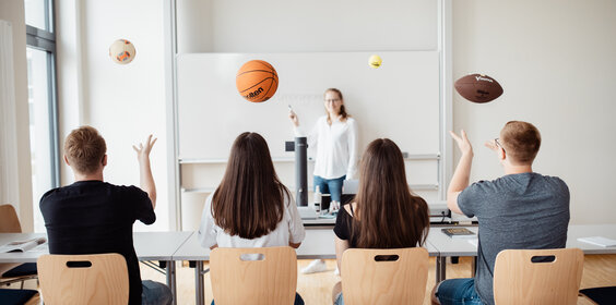 Studierende werfen einen Basketball, Football und Tennisball in die Luft