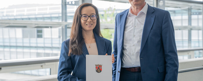 Eine Frau und ein Mann stehen zusammen. Die Dame hält eine Urkunde in der Hand.