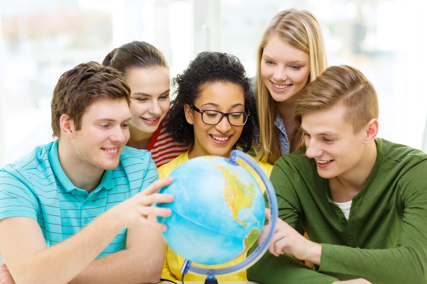 Fünf lächelnde Studierende schauen sich einen Globus an
