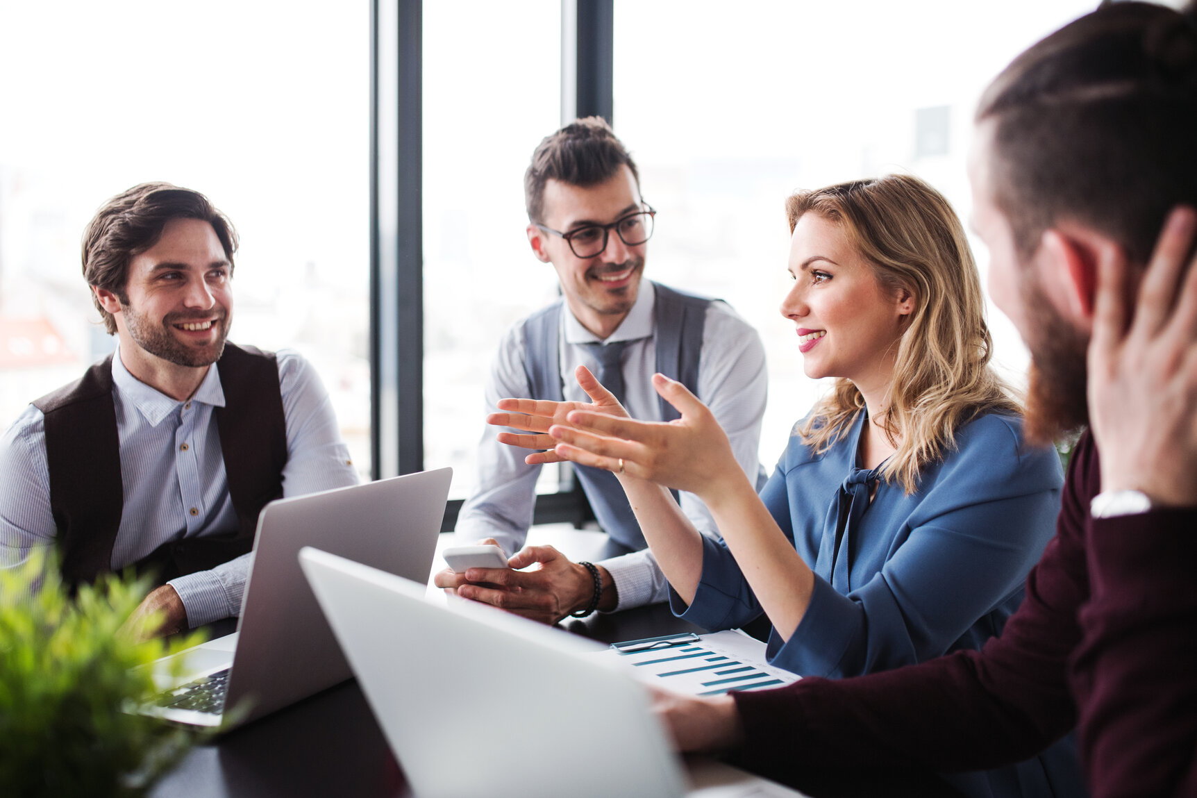 A group of young business people with laptop sitting in an office, talking.