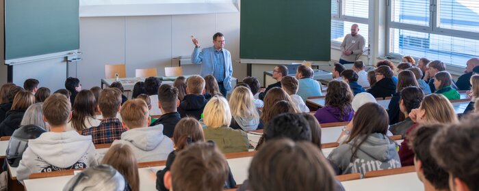 Interessierte im Hörsaal bei einer Begrüßung durch einen Mann