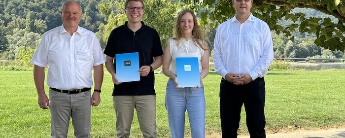 Eine Gruppe von vier Personen steht auf einer Wiese. Die Preisträgerin und der Preisträger halten ihre Urkunde in der Hand. 