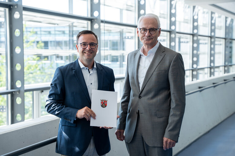 Zwei Männer stehen zusammen. Der linke von beiden hält eine Urkunde in der Hand.