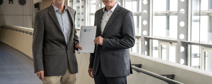 Zwei Männer stehen nebeneinander und halten gemeinsam eine Urkunde.