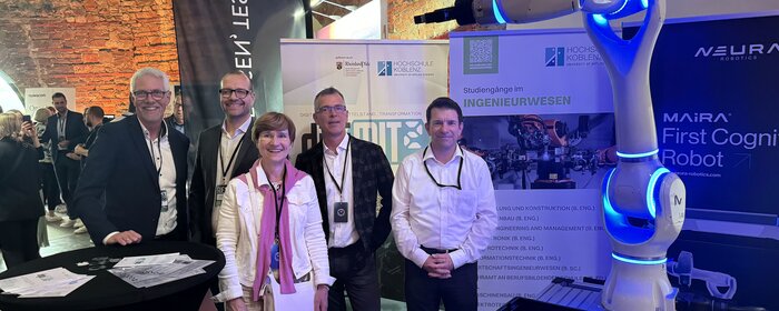 Eine Gruppe von vier Männern und einer Frau auf der Messe mit einem Roboter