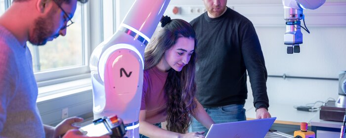 Zwei Männer und eine Frau in einem Labor mit Roboterarm.