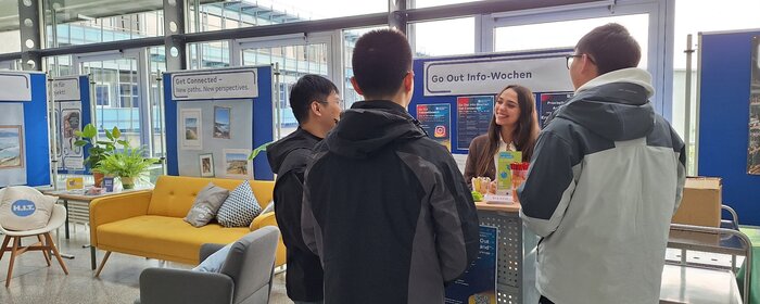 Drei Studierende stehen bei einer Beraterin des International Office am Infostand.